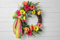 Handmade bright floral wreath with pink, yellow, and green flowers and a colorful striped bow, perfect for spring and summer front door decor.