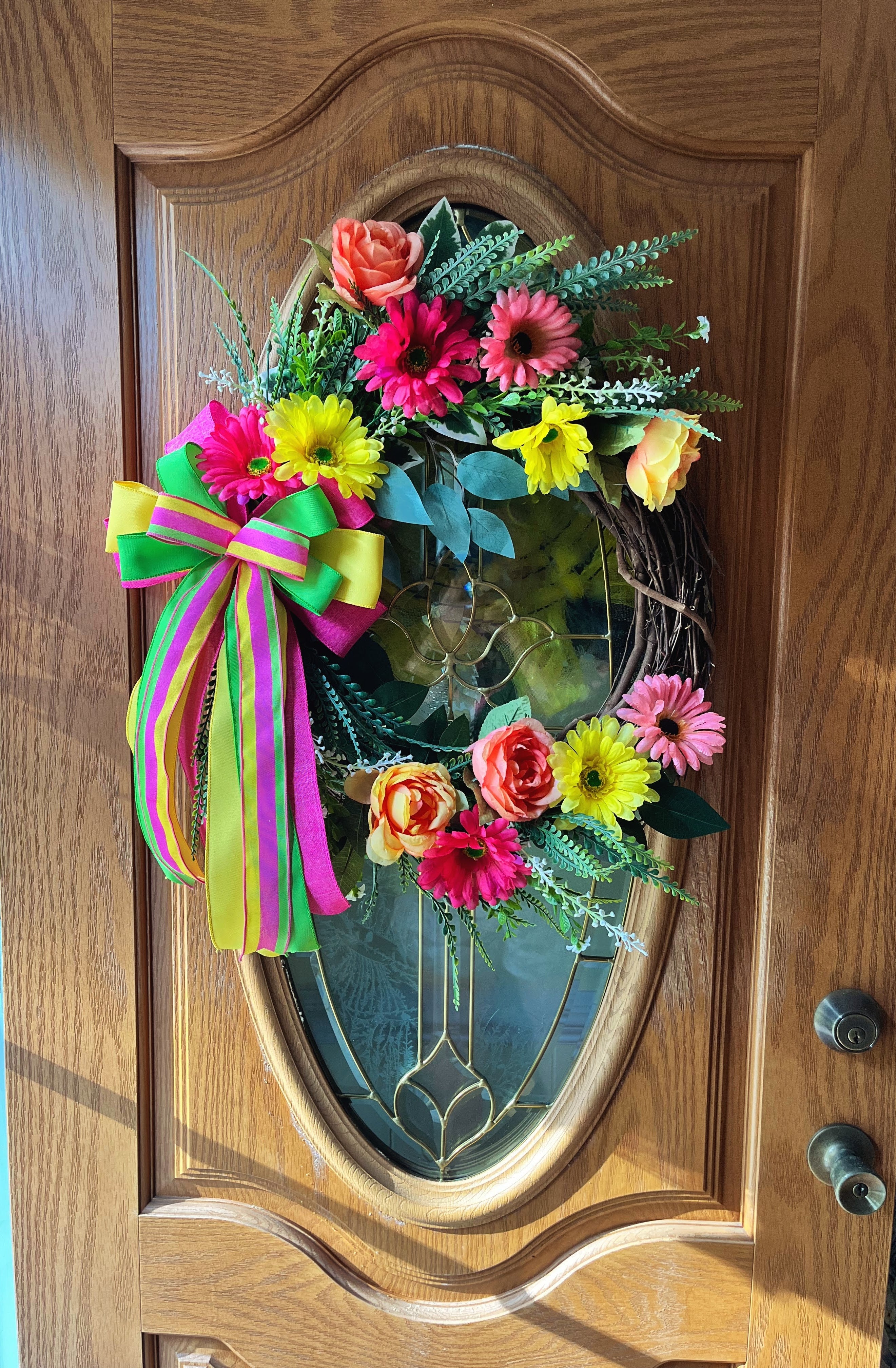 Handmade bright floral wreath with pink, yellow, and green flowers and a colorful striped bow, perfect for spring and summer front door decor.