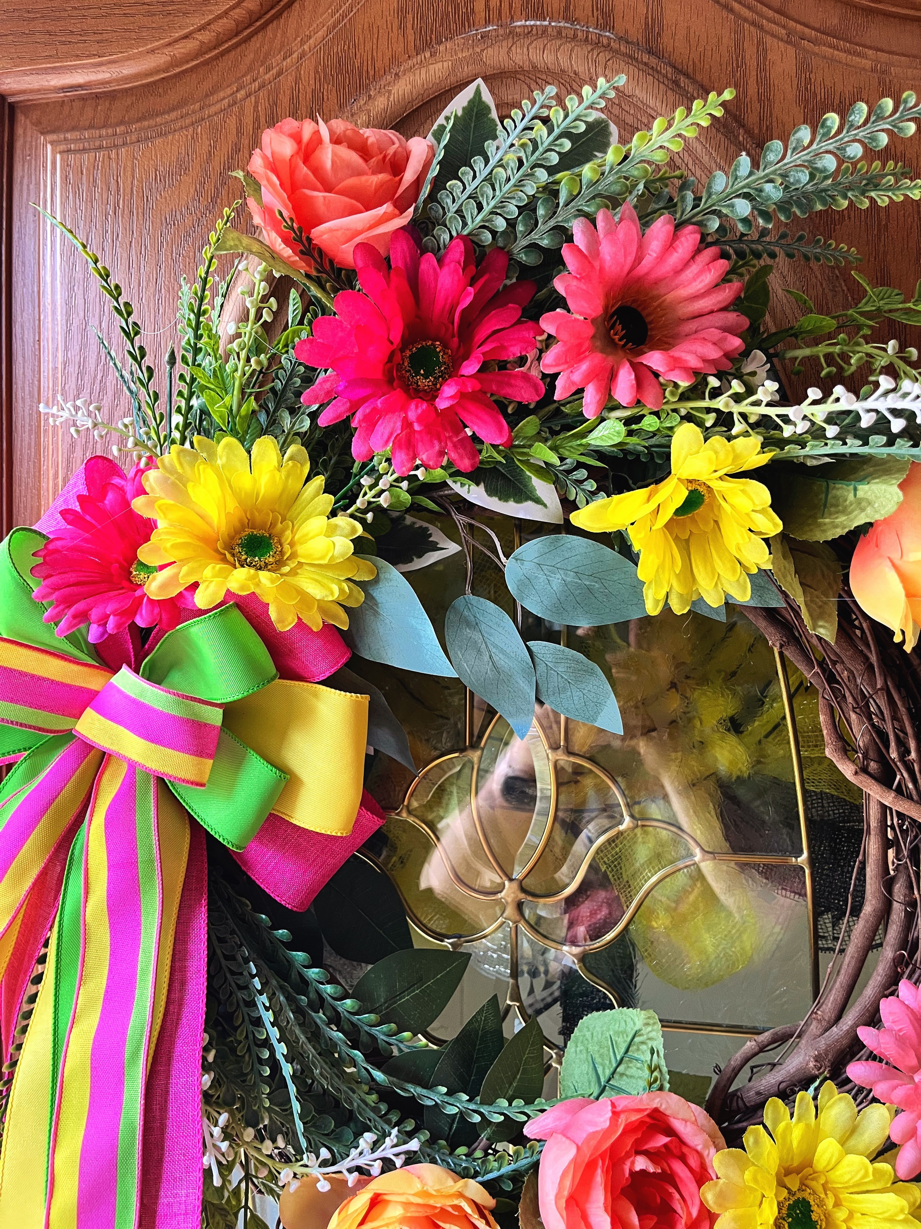 Handmade bright floral wreath with pink, yellow, and green flowers and a colorful striped bow, perfect for spring and summer front door decor.
