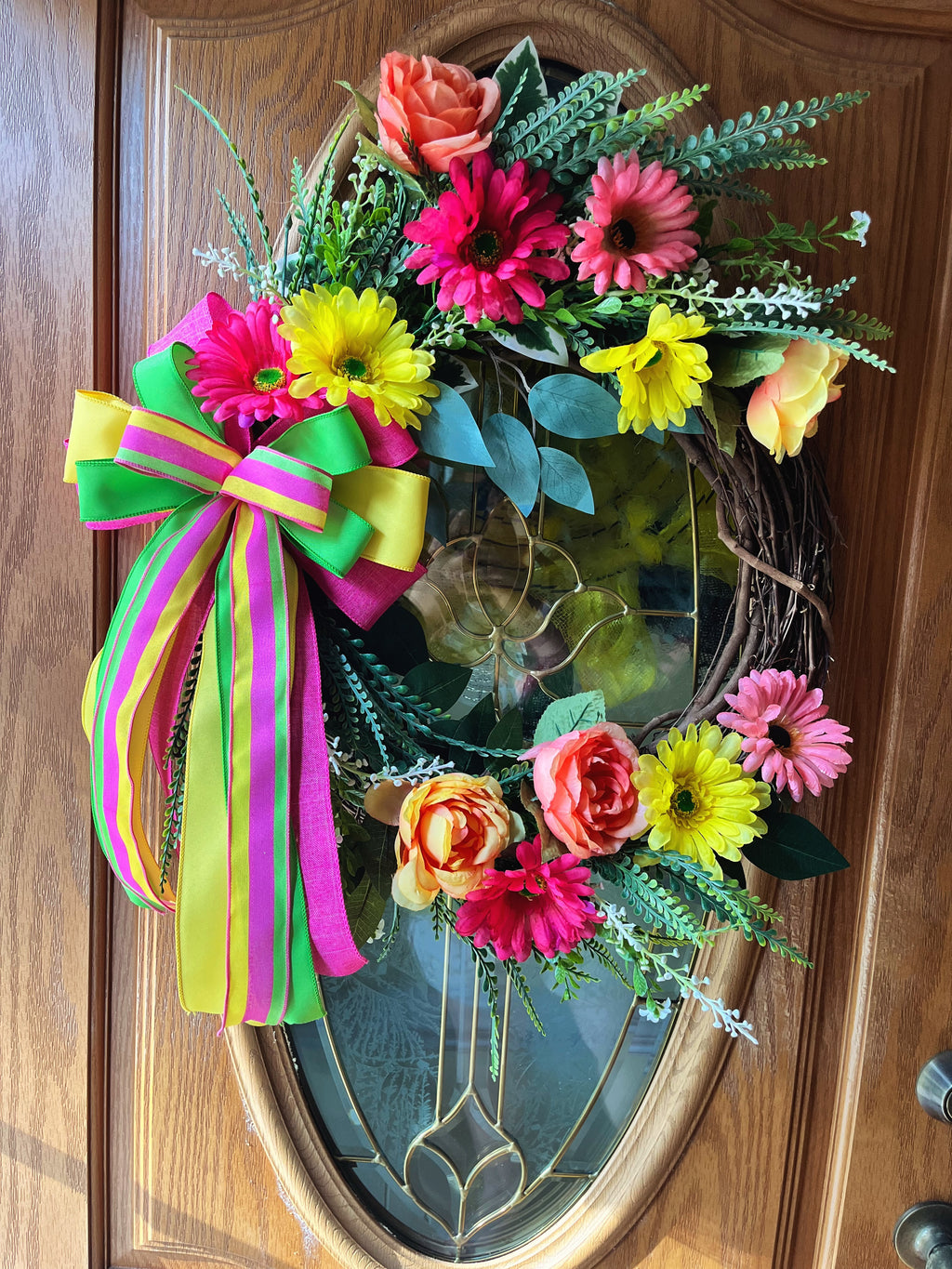 Handmade bright floral wreath with pink, yellow, and green flowers and a colorful striped bow, perfect for spring and summer front door decor.