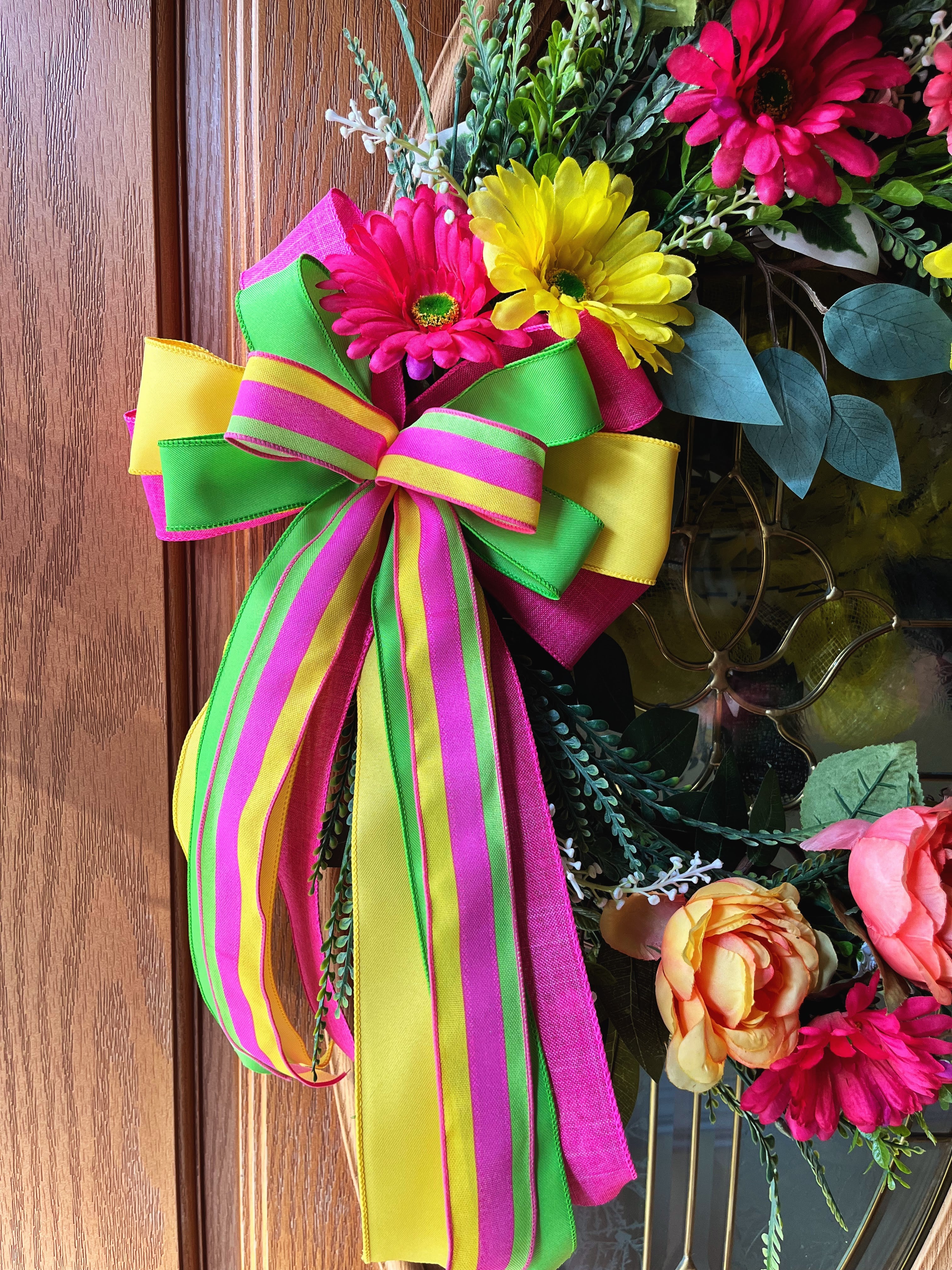 Handmade bright floral wreath with pink, yellow, and green flowers and a colorful striped bow, perfect for spring and summer front door decor.