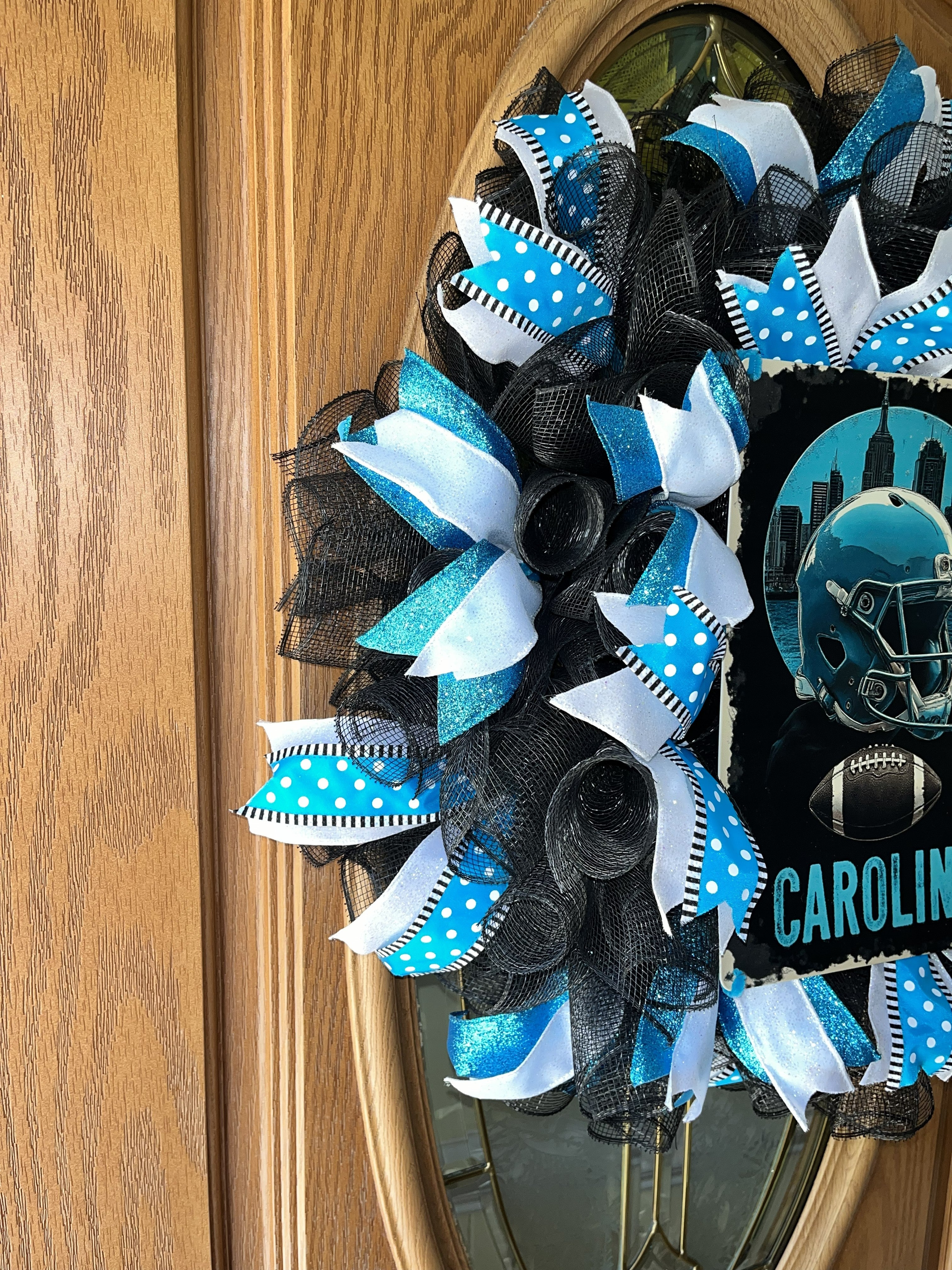 “Handmade Carolina football wreath featuring black, blue, and white mesh ribbon with a helmet and football sign, perfect for sports fan front door decor