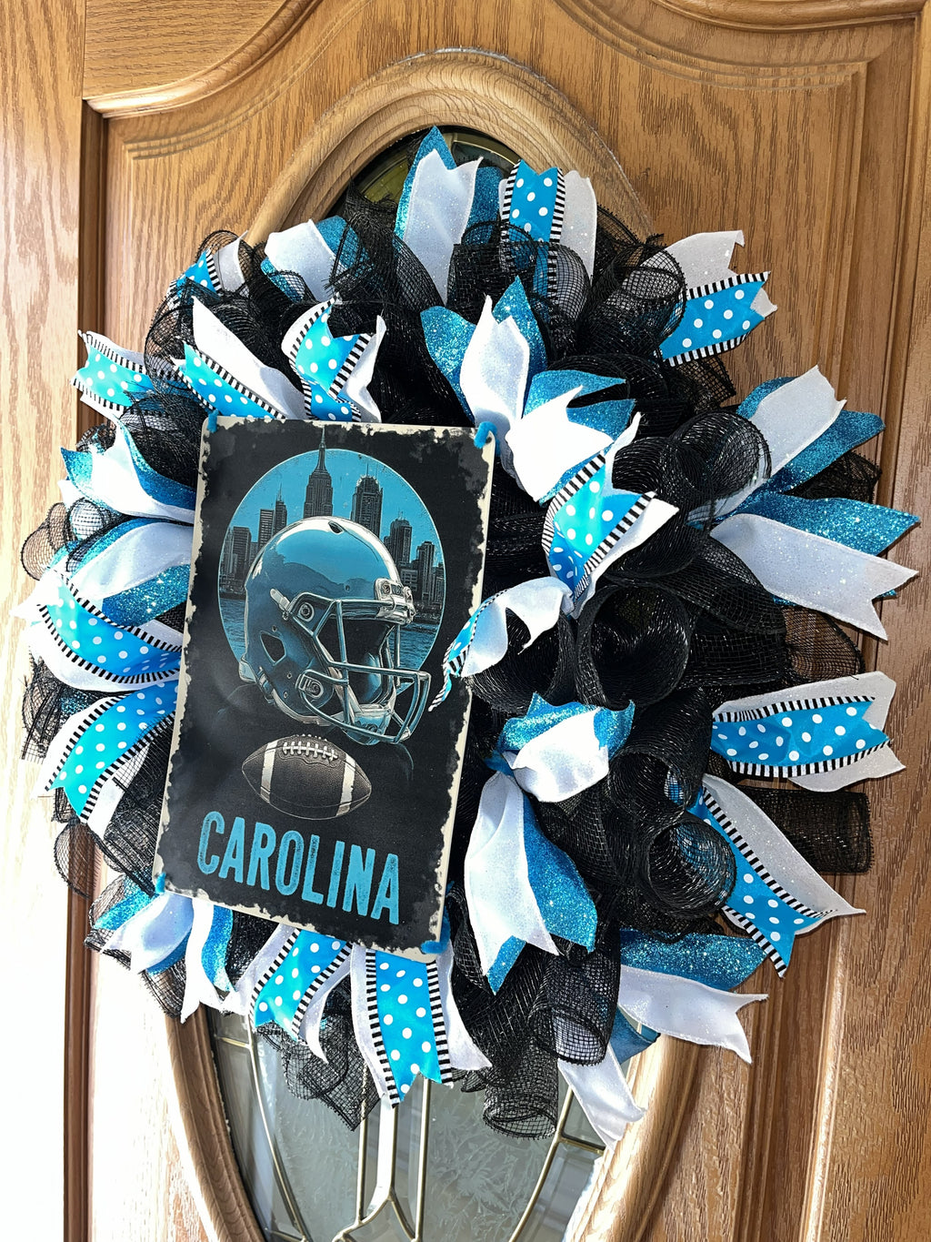 “Handmade Carolina football wreath featuring black, blue, and white mesh ribbon with a helmet and football sign, perfect for sports fan front door decor