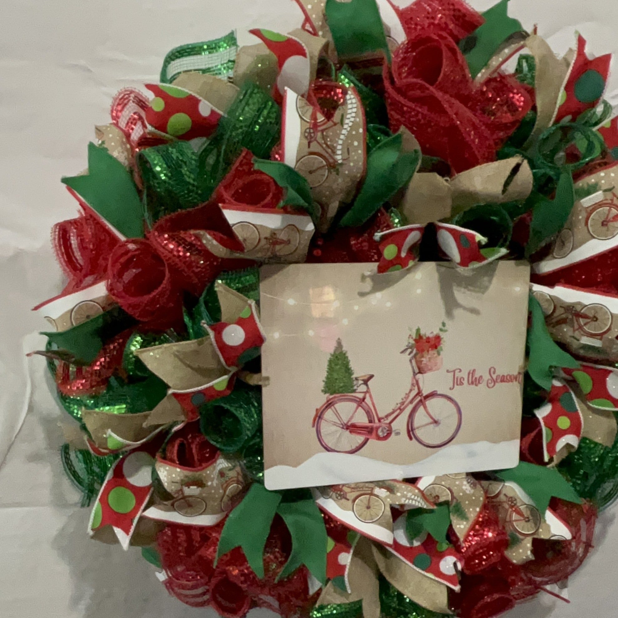 Handmade Christmas wreath with red and green mesh ribbon, featuring a vintage bicycle ‘Tis the Season’ sign for festive holiday front door decor.