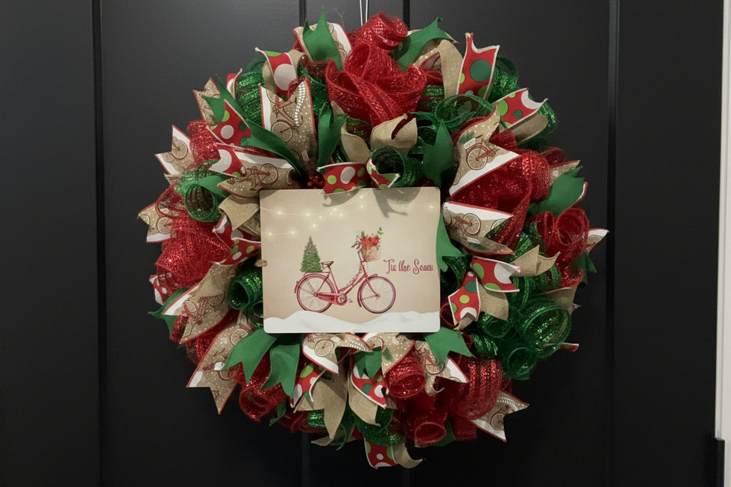 Handmade Christmas wreath with red and green mesh ribbon, featuring a vintage bicycle ‘Tis the Season’ sign for festive holiday front door decor.