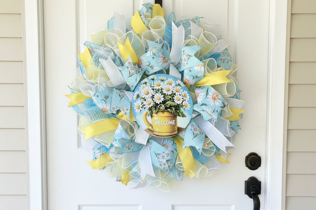 Handmade spring and summer wreath with blue and yellow mesh ribbon, featuring a daisy-filled welcome sign for cheerful front door decor.