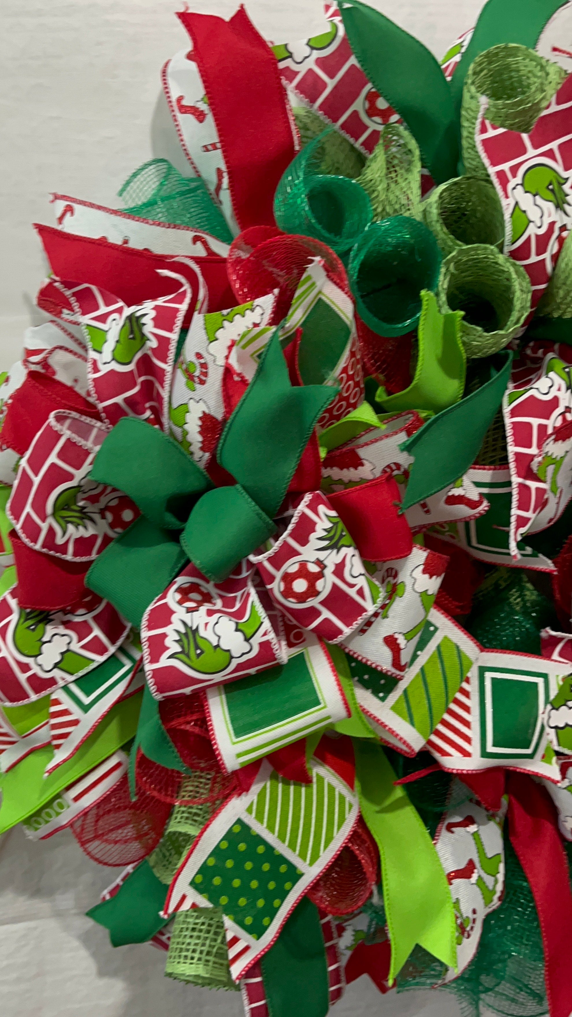 Handmade red and green Christmas wreath with a whimsical Grinch-inspired face sign, featuring festive ribbon and mesh for holiday front door decor