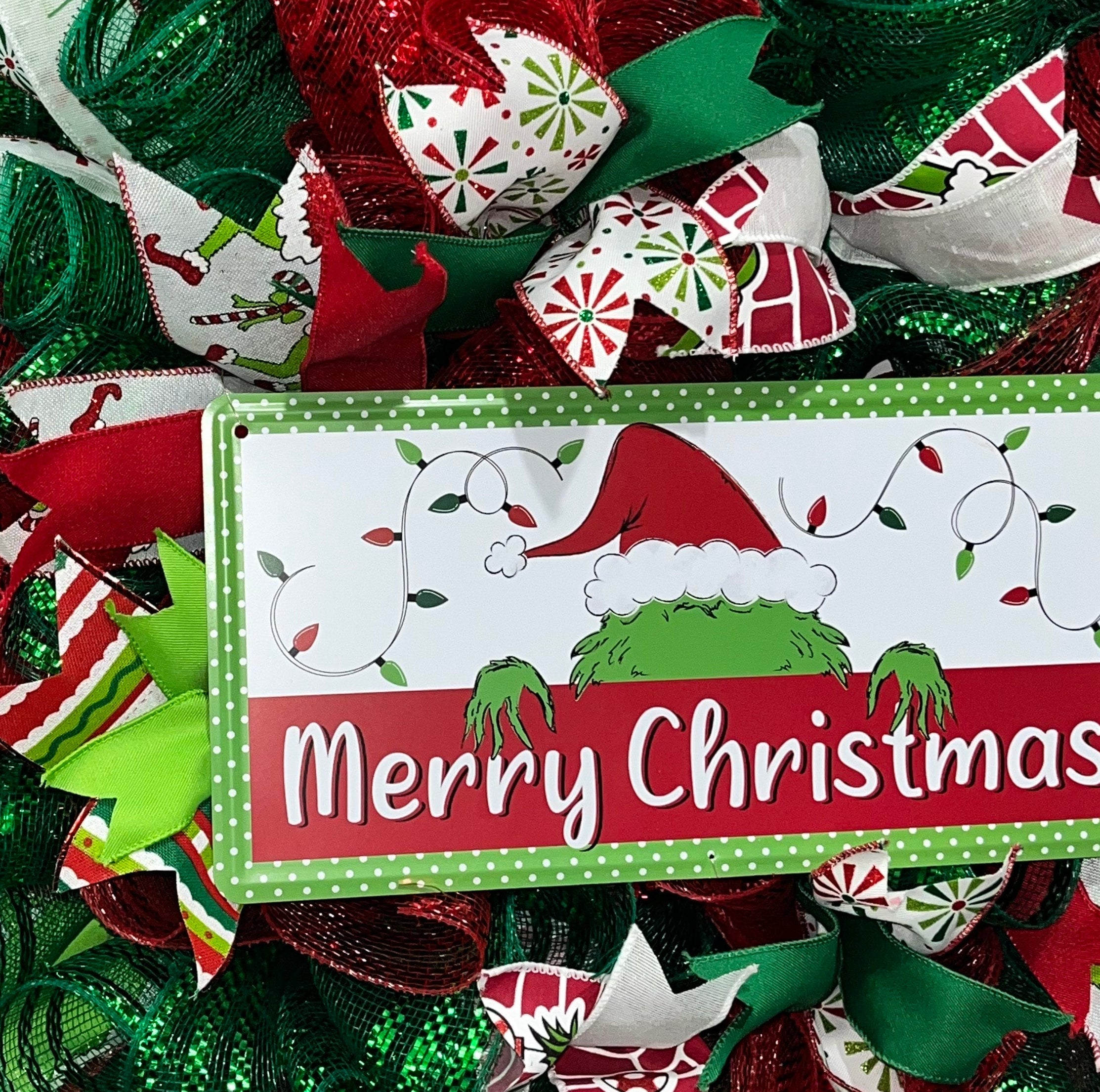 Handmade red and green Christmas wreath with a ‘Merry Christmas’ sign and whimsical Grinch-inspired design for festive front door decor.