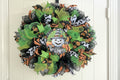 Halloween-themed wreath with green, black, and orange decorations on a white background
