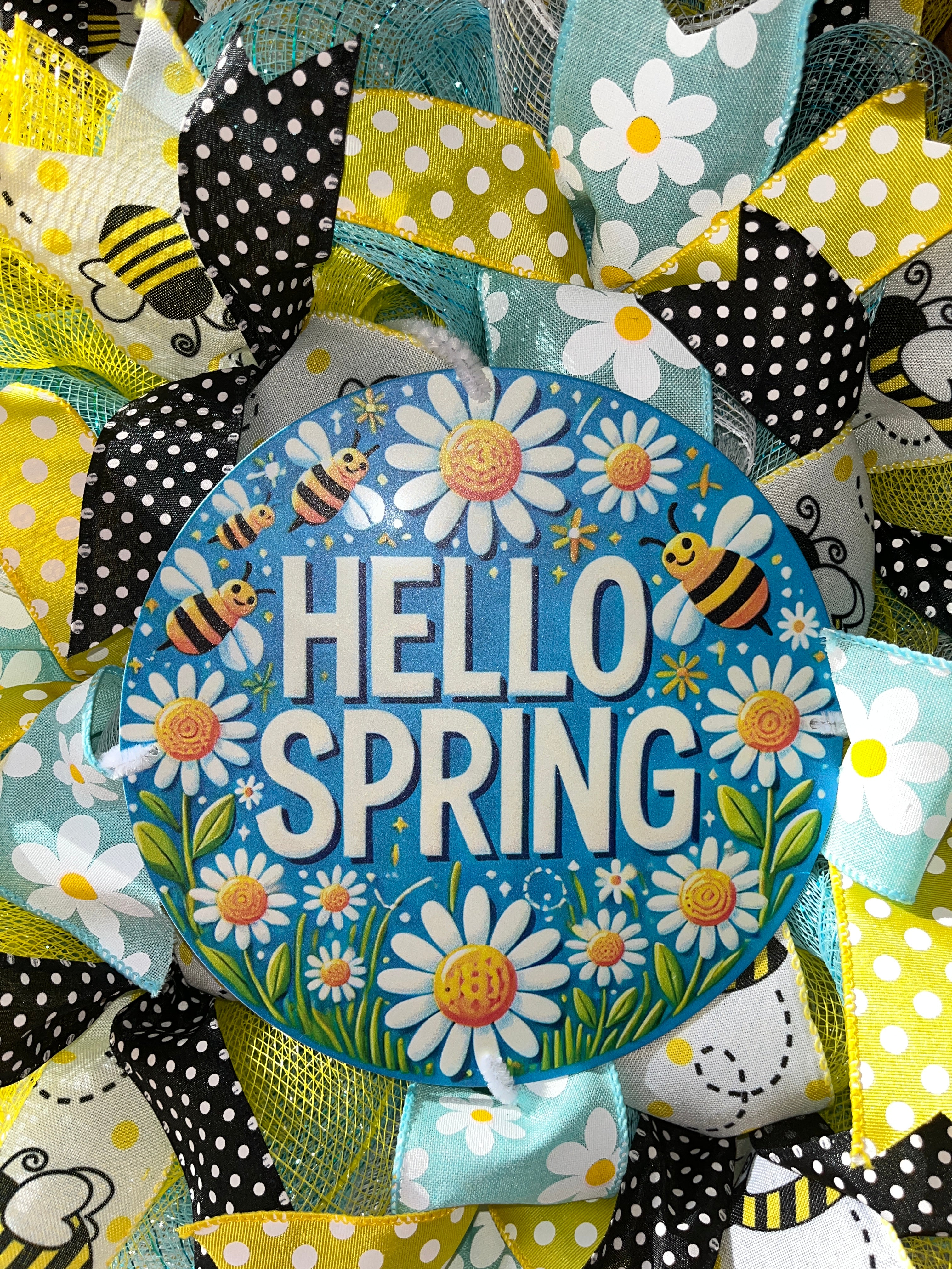 Colorful metal wreath sign with 'Hello Spring' text, flowers, and bees.