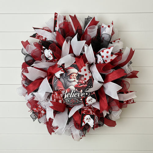 Handmade Christmas deco wreath with red, white, and black ribbons and Santa Claus "Believe" centerpiece.