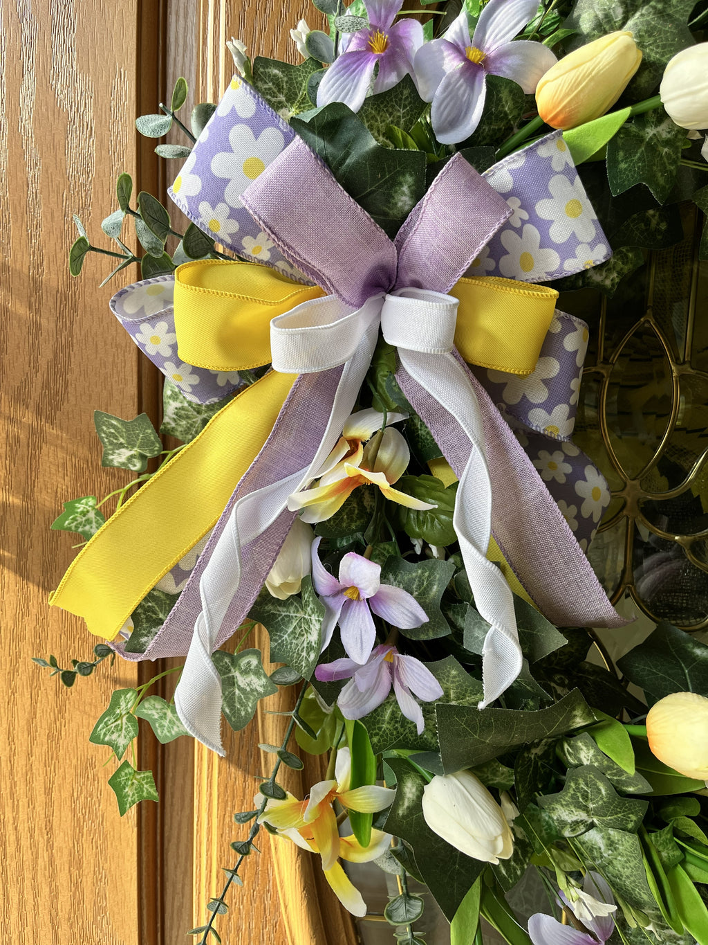 Handmade spring wreath with pastel tulips and florals in lavender, yellow, and white, featuring greenery and a decorative bow for front door decor.