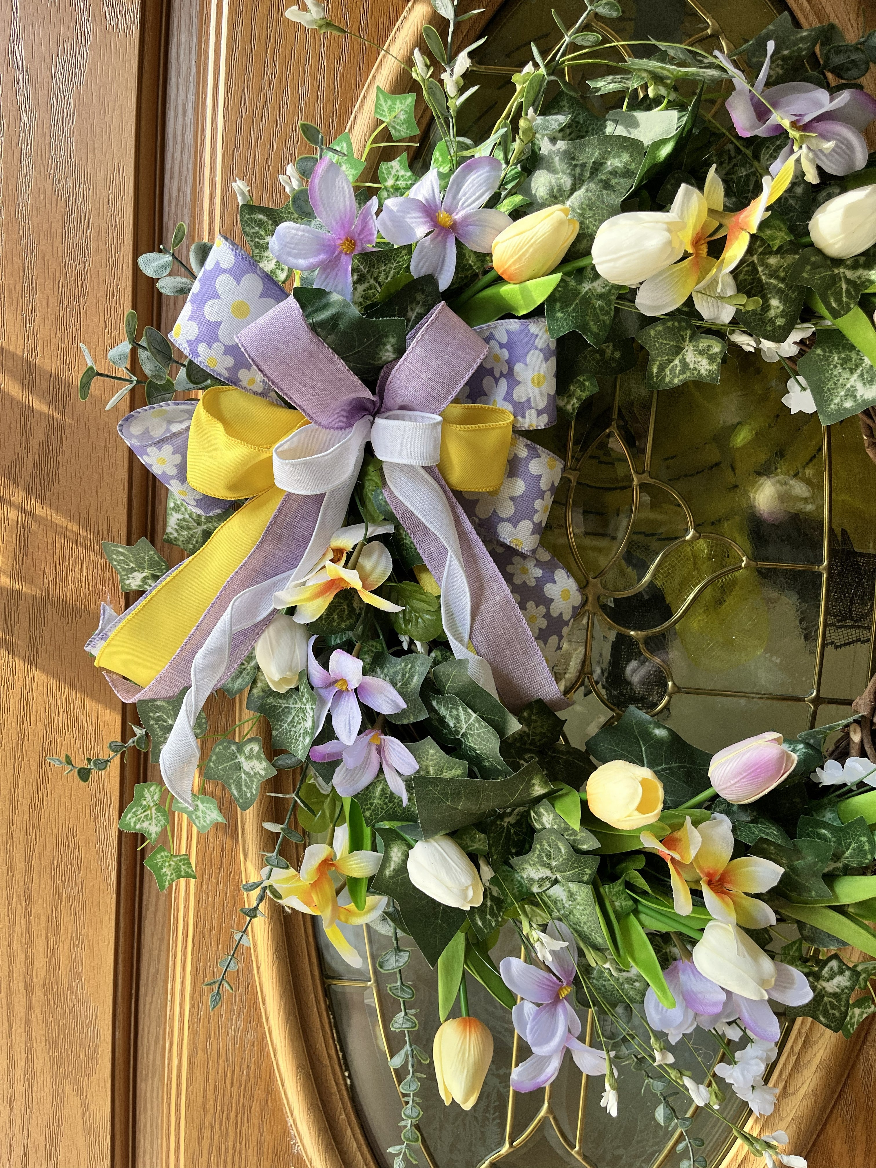 Handmade spring wreath with pastel tulips and florals in lavender, yellow, and white, featuring greenery and a decorative bow for front door decor.