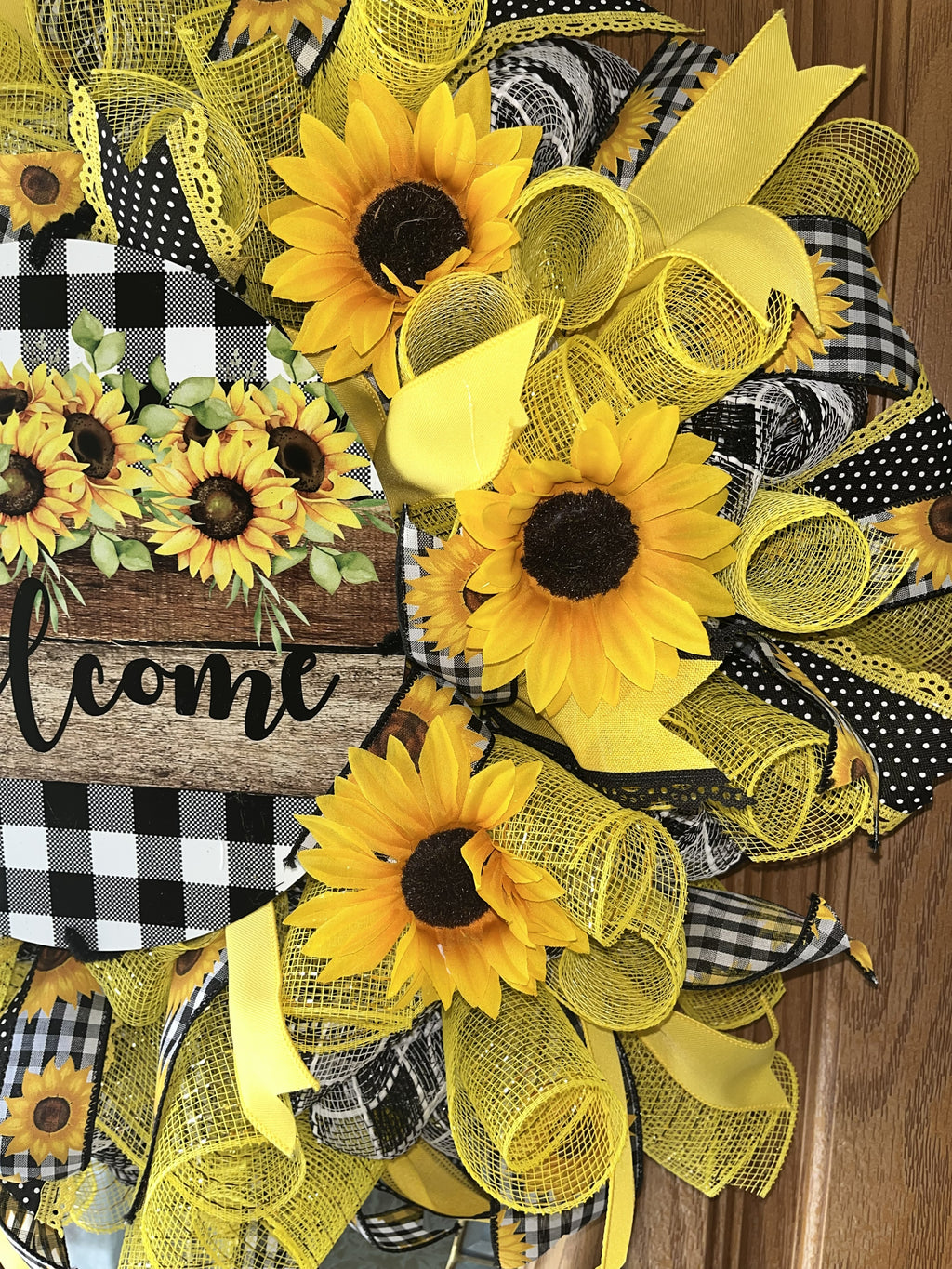 Handmade sunflower wreath with black and white buffalo check ribbon and a welcome sign, featuring bright yellow sunflowers for farmhouse front door decor.
