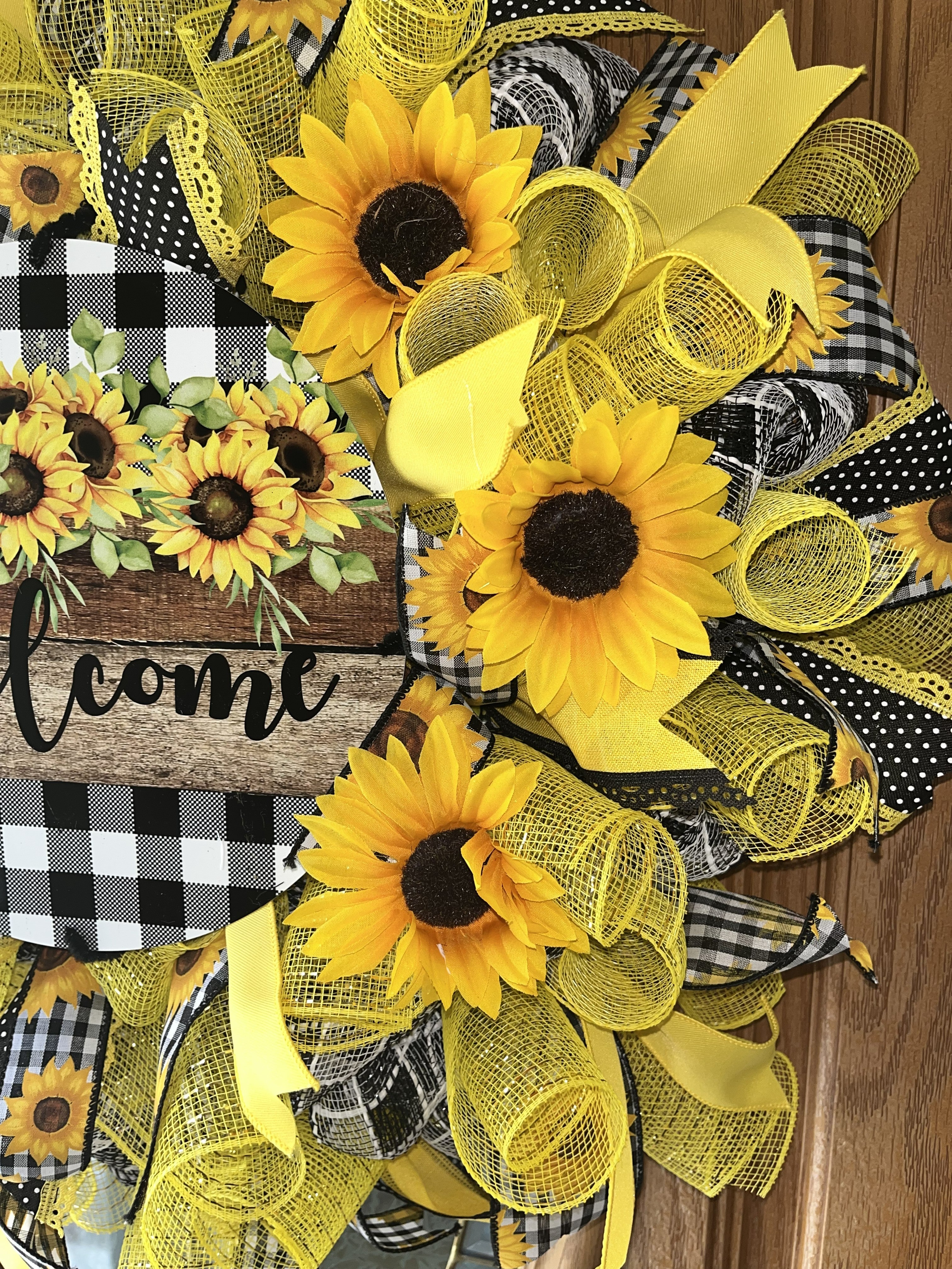 Handmade sunflower wreath with black and white buffalo check ribbon and a welcome sign, featuring bright yellow sunflowers for farmhouse front door decor.