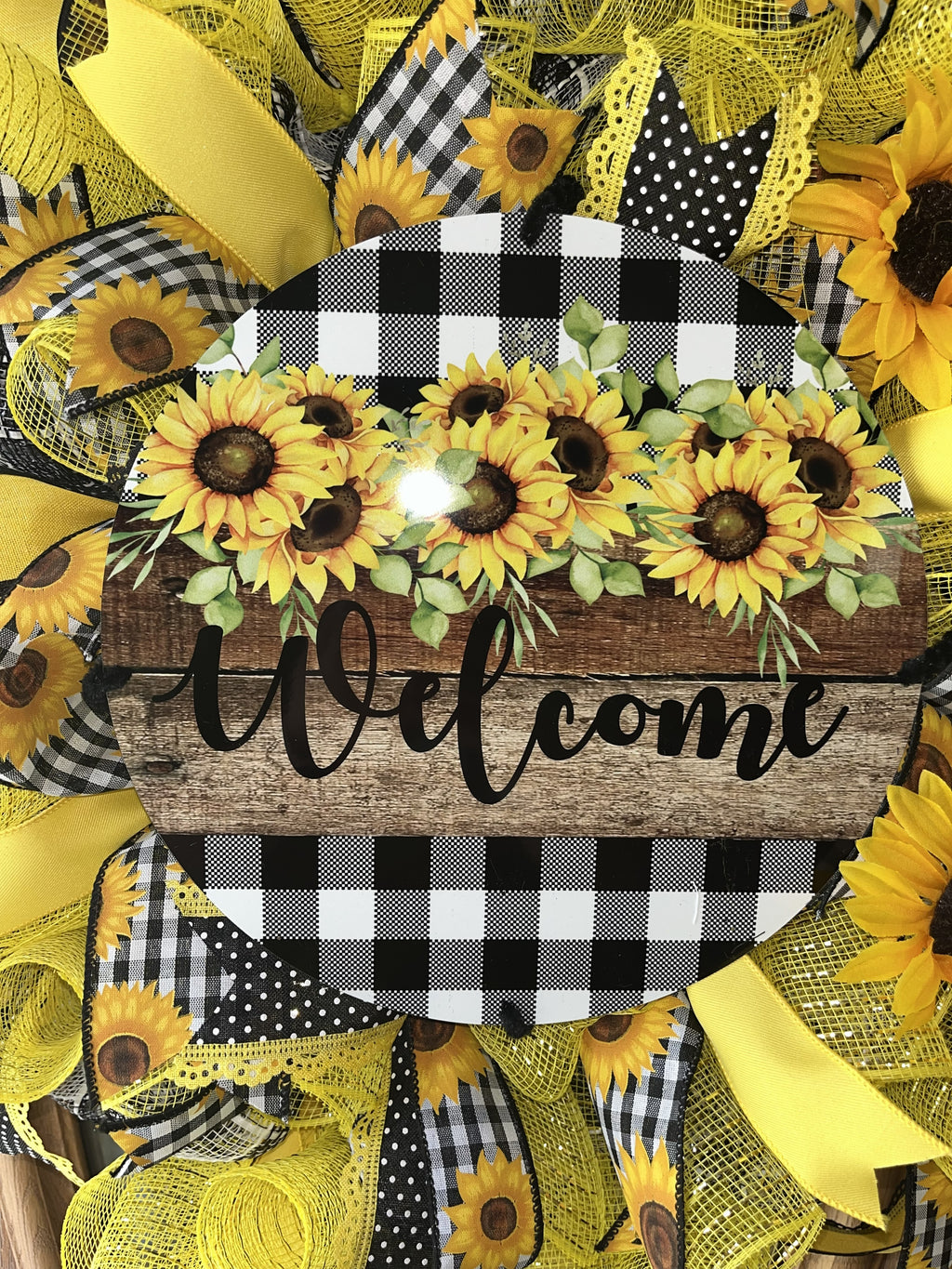 Handmade sunflower wreath with black and white buffalo check ribbon and a welcome sign, featuring bright yellow sunflowers for farmhouse front door decor.
