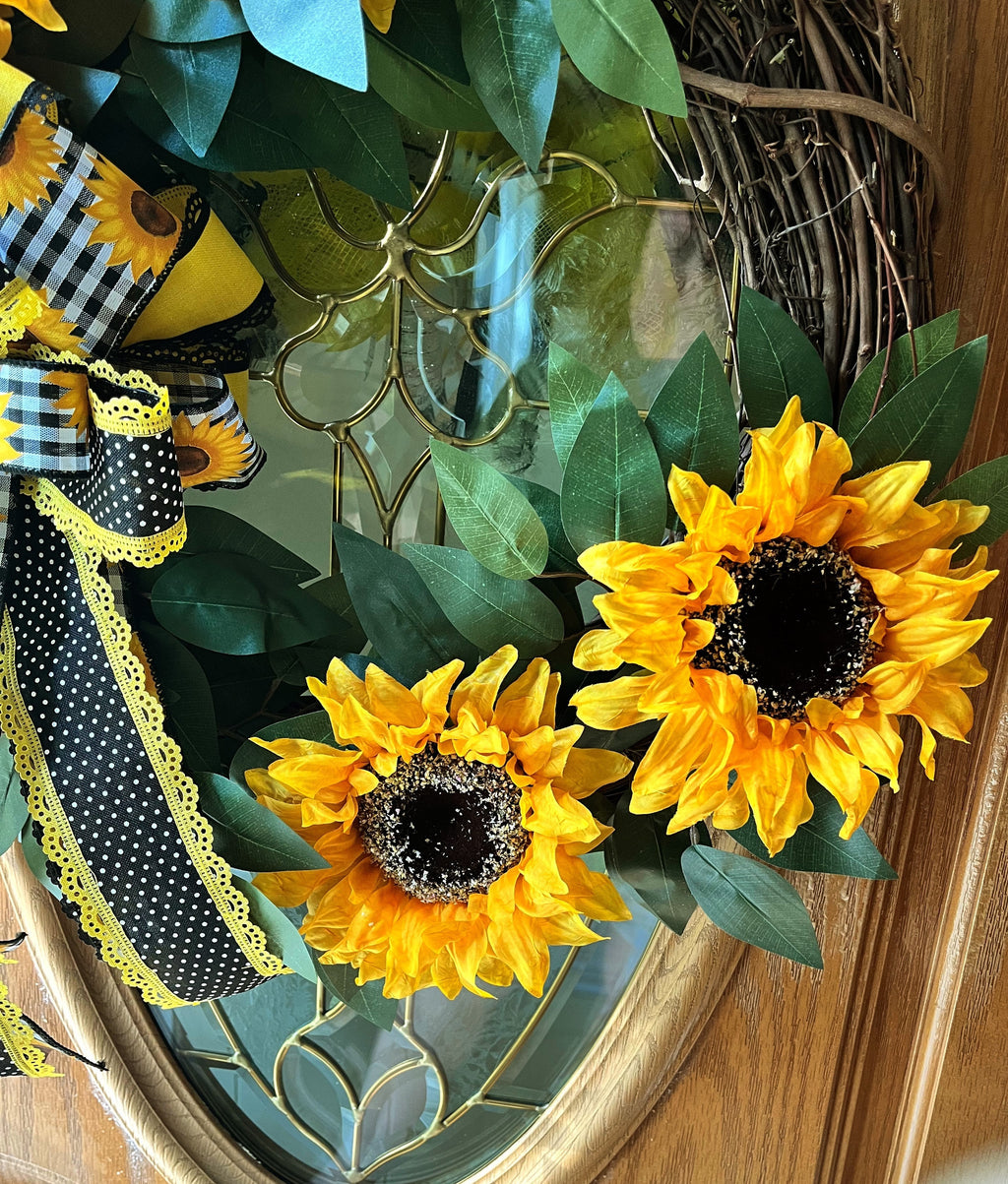 Handmade sunflower wreath with bright yellow sunflowers, greenery, and a black and yellow buffalo check bow for farmhouse summer front door decor.