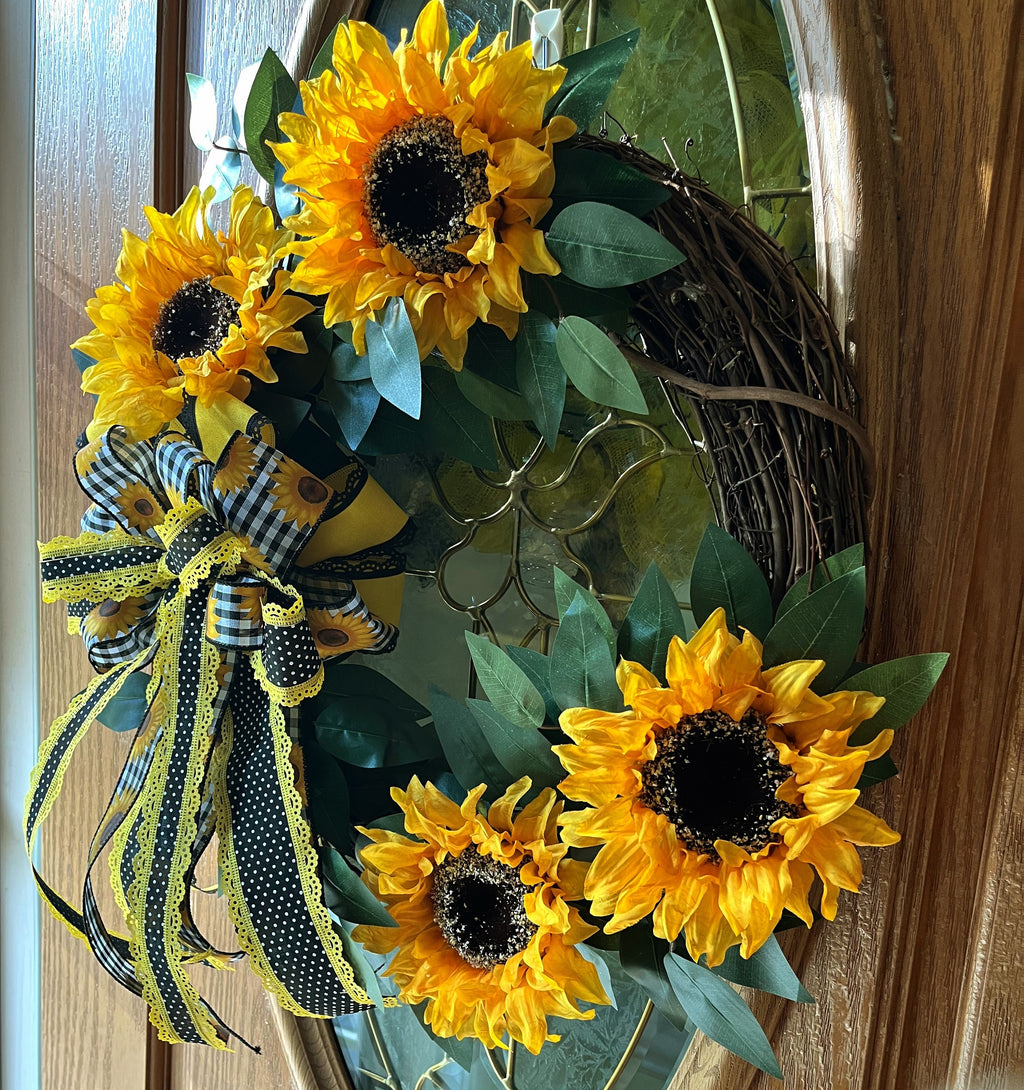 Handmade sunflower wreath with bright yellow sunflowers, greenery, and a black and yellow buffalo check bow for farmhouse summer front door decor.
