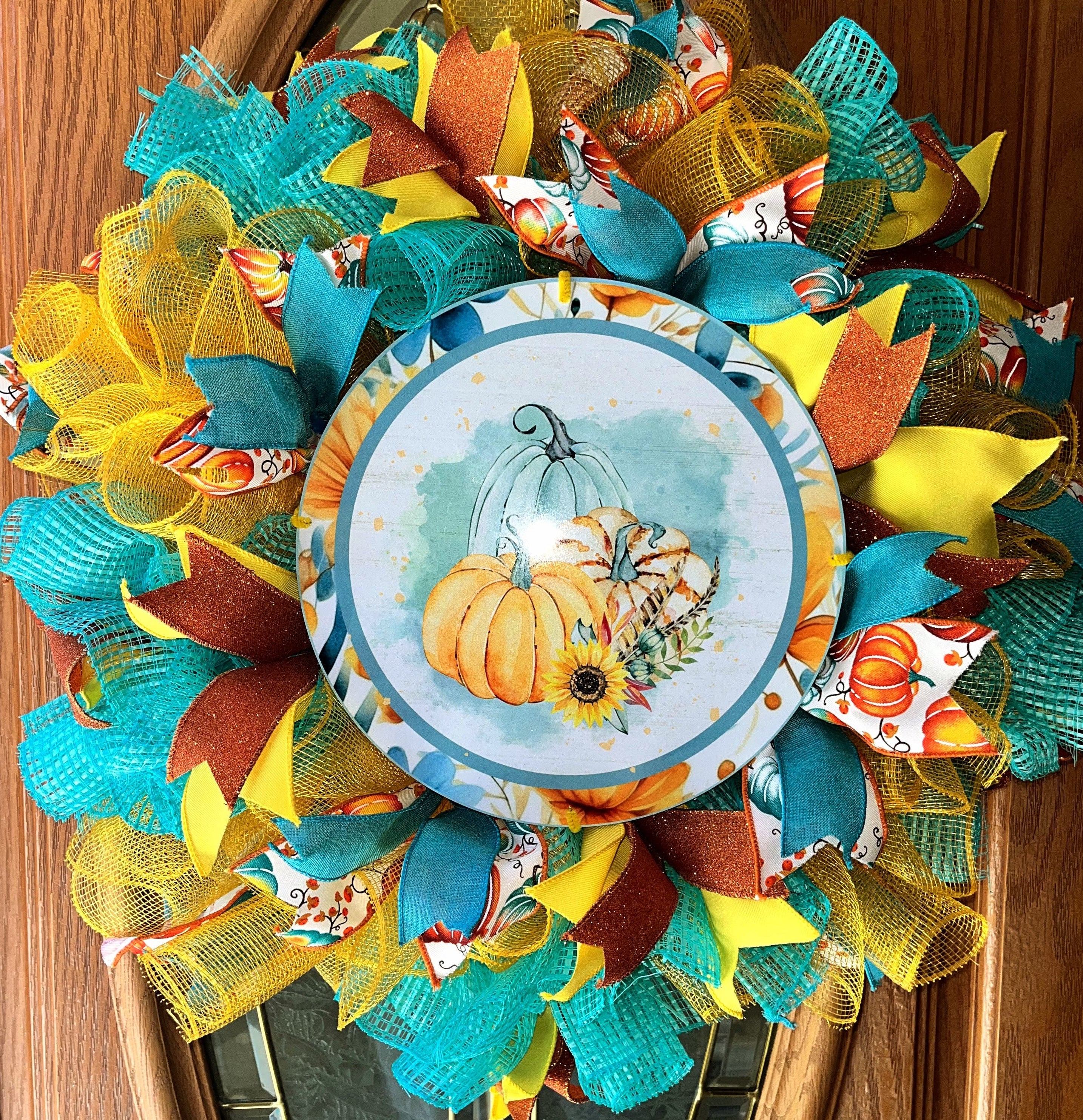 Handmade fall wreath featuring teal, yellow, and orange mesh with a pumpkin sign, perfect for unique autumn front door decor.