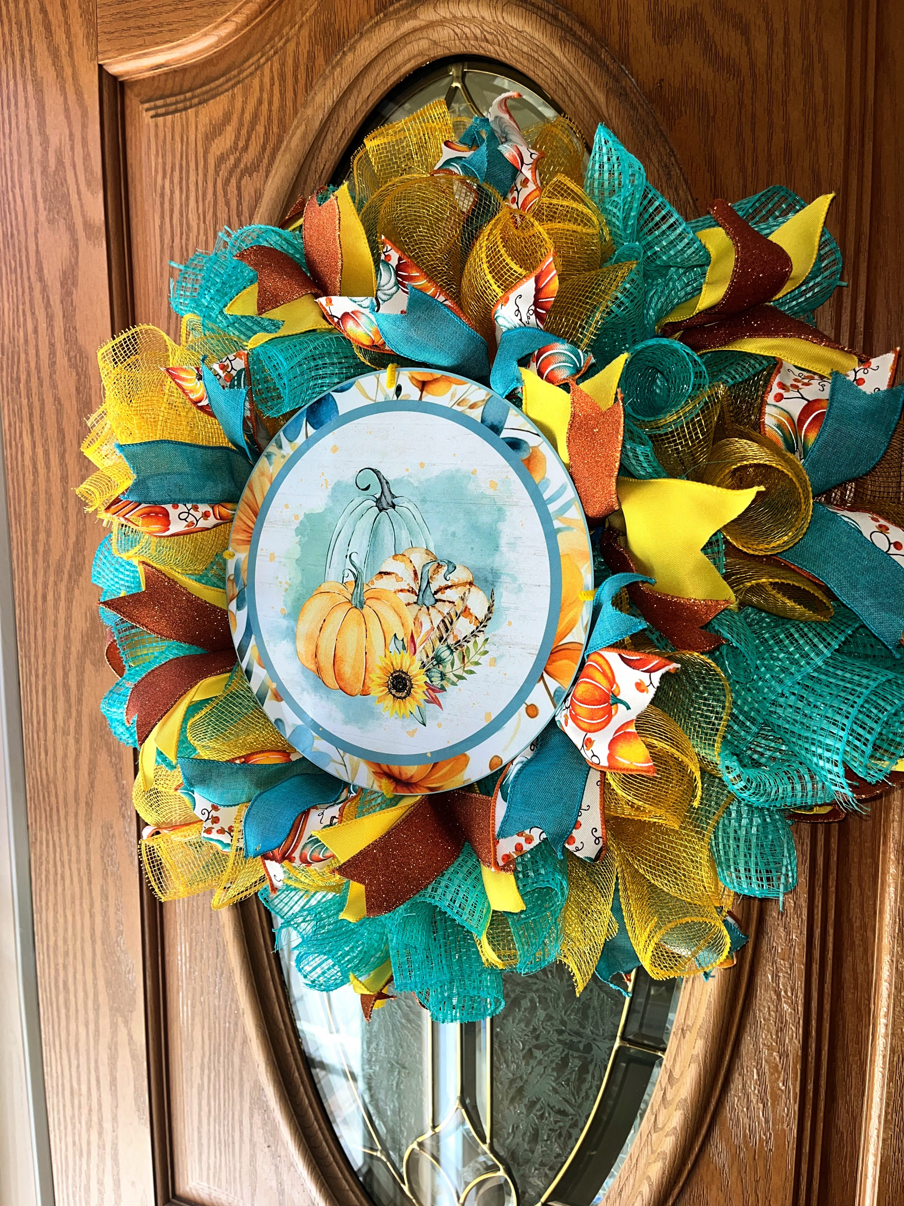 Handmade fall wreath featuring teal, yellow, and orange mesh with a pumpkin sign, perfect for unique autumn front door decor.