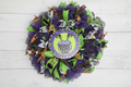 Colorful Halloween-themed wreath with purple, green, and orange decorations on a white tiled wall.